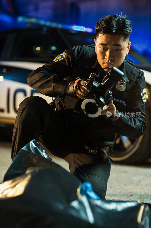 图为一名亚洲警察在犯罪现场对装在尸袋里的受害人尸体拍照。警局的年轻警探破获了他的第一起谋杀案