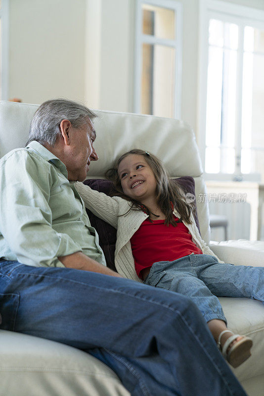 一位老人在家里的沙发上和他的孙女愉快地交谈