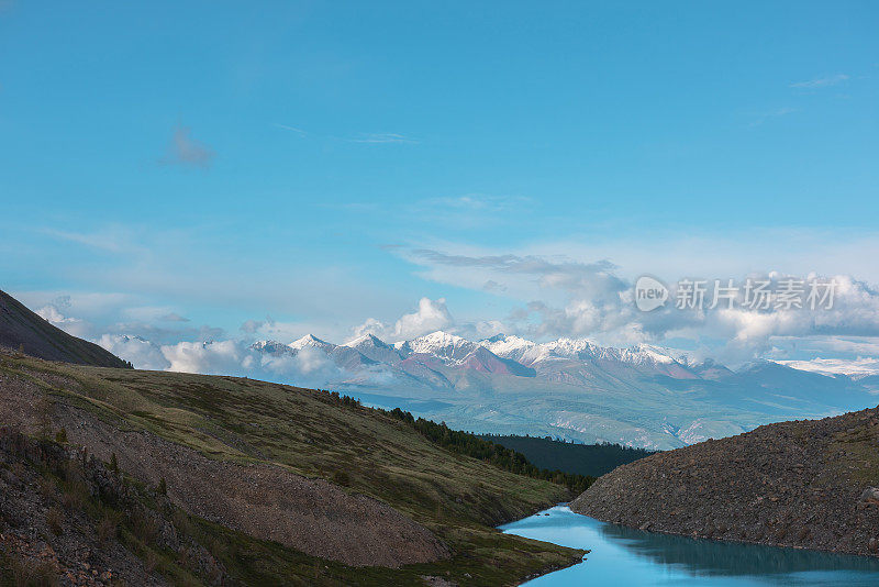 大气景观，湛蓝的山湖与高雪白色山脉在阳光下的低云。引人注目的夜景到高山湖泊和大的阳光照耀的雪山在低云。