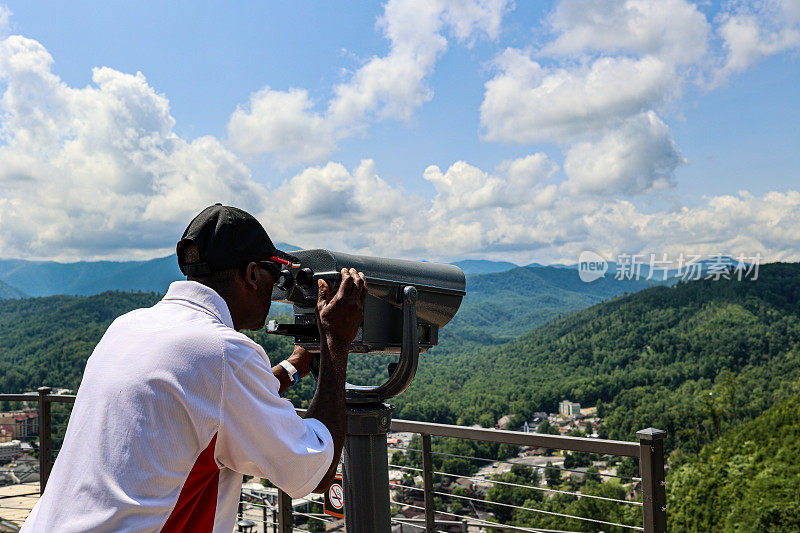 一幅黑人男子通过投币式望远镜看山的画像