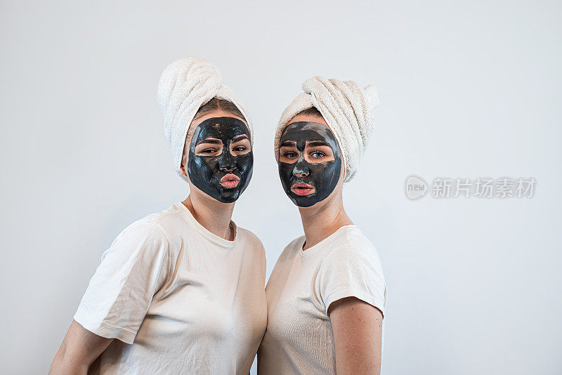 两个姐妹或女友的肖像使皮肤面膜隔离在白色上