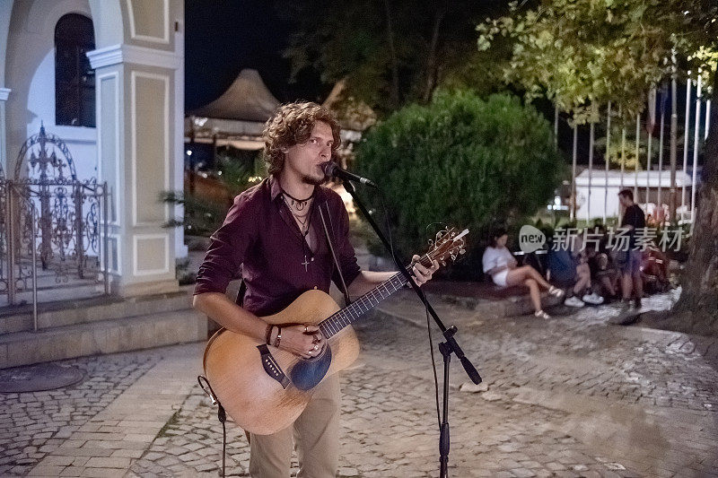 深夜，街头艺人在街上唱着歌，弹着吉他。