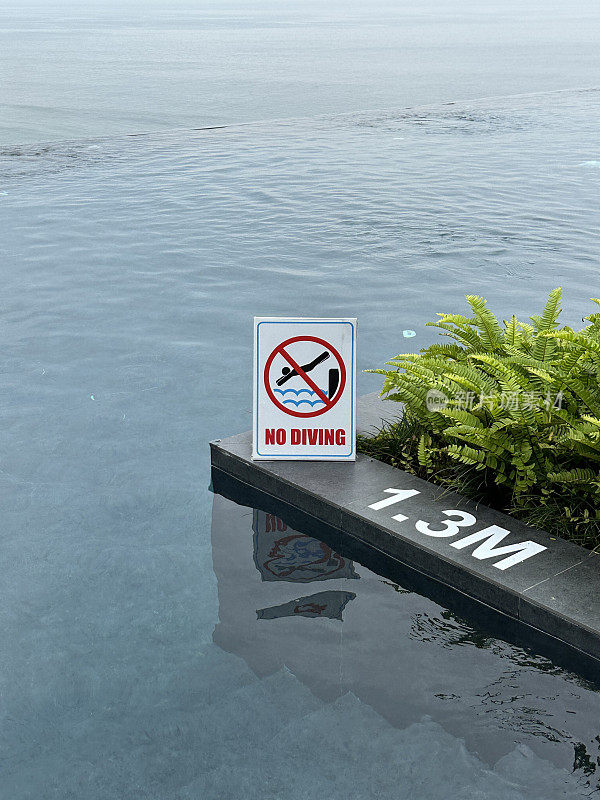 “禁止潜水”标志的图像，建议a框夹心板，在室外闪亮的抛光混凝土泳池边，无限游泳池深度标记，重点在前景
