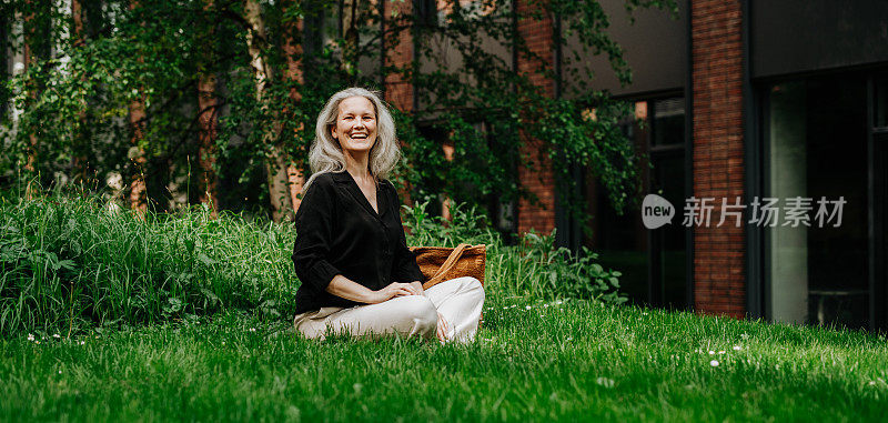一个美丽的白发女人坐在城市公园的草地上，面带微笑。