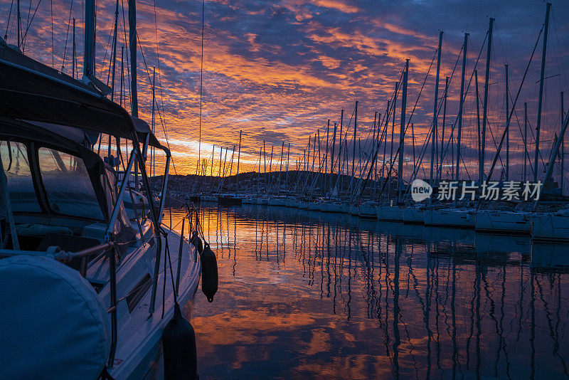 夕阳下停泊在港口的帆船，红色的天空和水面上帆船的倒影。