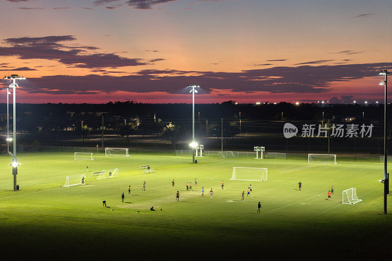 日落时分，人们在灯火通明的公共体育场踢足球。积极的生活方式理念