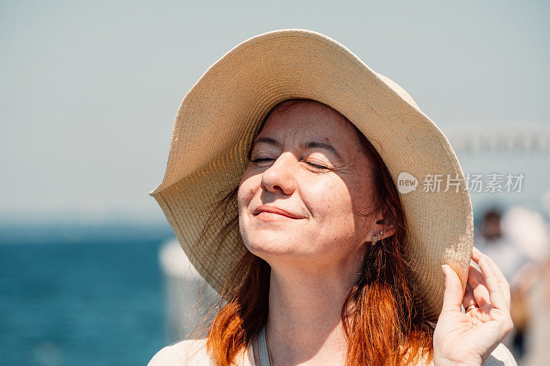一个红头发的女人闭着眼睛享受着宁静的时刻，阳光照在她的脸上