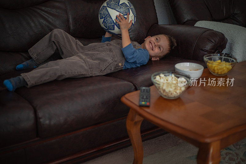 一个小男孩正在家里看电视上的足球比赛