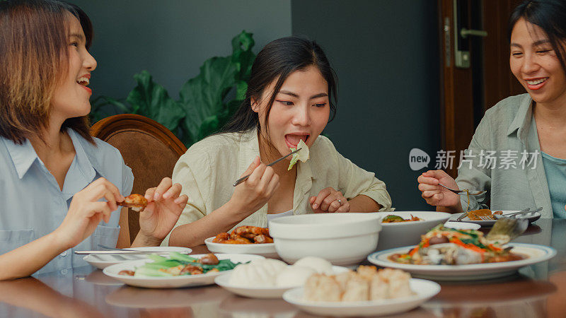 年轻的亚洲家庭准备中国菜，坐在后院的餐桌上玩得很开心。多代同堂的家庭一起享受消费。