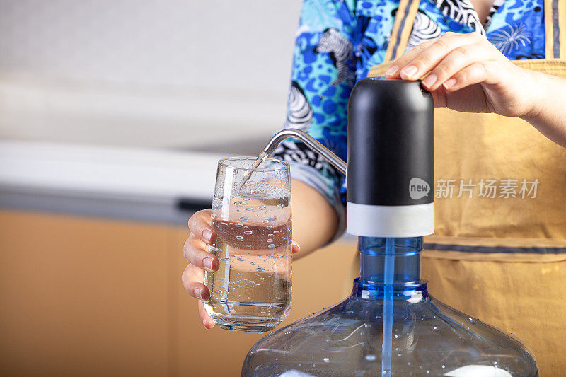 一个女人用电动水泵，自动饮水机把水倒进杯子里。