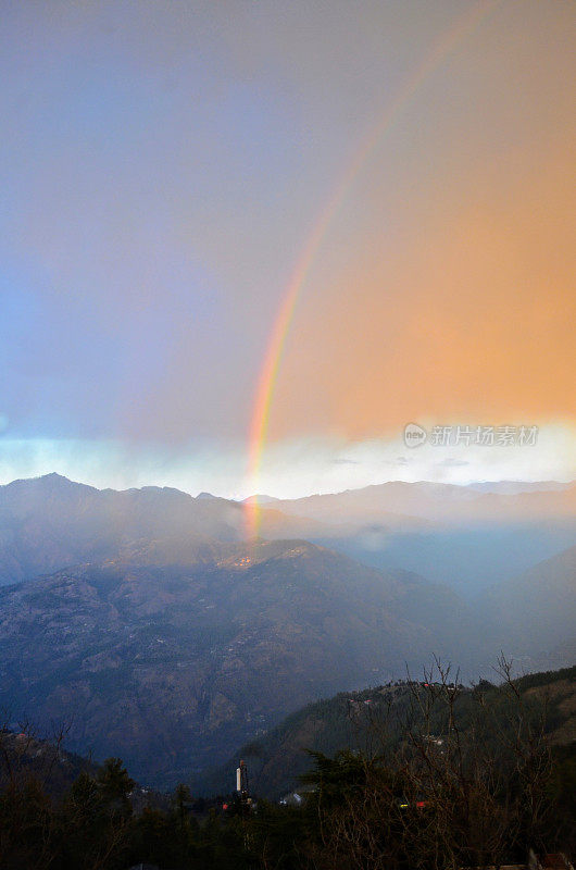 由于雨后的阳光，天空中出现了彩虹。山、谷、树、房子和云。山站西姆拉，喜马偕尔邦，印度，亚洲。自然自然现象。自然摄影之美。
