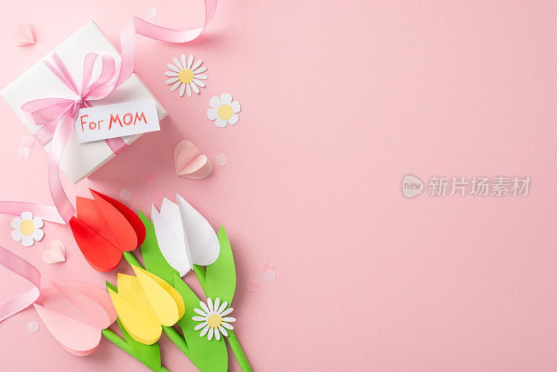 DIY母亲节概念，纸郁金香，洋甘菊，一个自制的礼盒，上面写着“给妈妈”，系着丝带，在粉红色画布上的纸心和细纸彩中