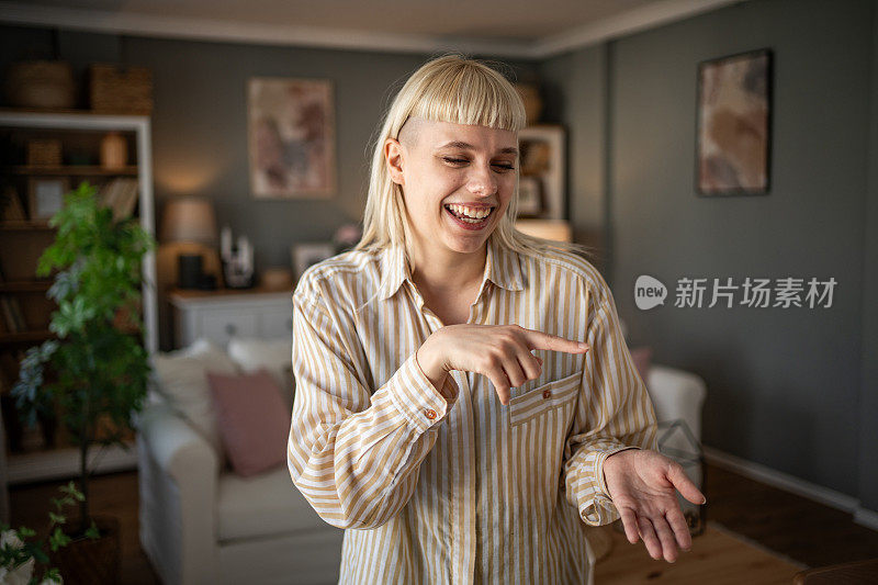 一名年轻女子站在客厅里为她的视频博客拍摄视频，看着镜头，在社交媒体上与她的粉丝交谈