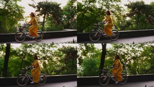 美丽微笑的女人穿着黄色长裙骑着一辆城市自行车，里面有一个篮子和鲜花在黎明。镜头光晕。替身。Slowmotion高清在线视频素材下载
