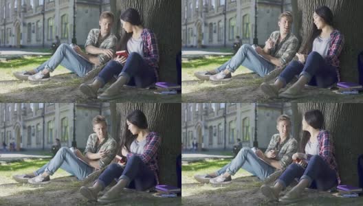 一个家伙从女孩的头发上取下枫树翅果，坐在他旁边的树下高清在线视频素材下载