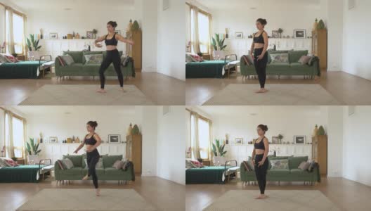 一个年轻的印度妇女在家训练，在明亮舒适的房间里做动感单车运动，穿着黑色上衣和打底裤。运动理念健康生活高清在线视频素材下载