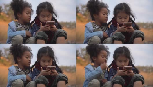不同的孩子朋友非洲裔美国人和亚洲女孩一起使用智能手机在自然的山上与阳光。一群孩子在花园公园用手机玩互联网。高清在线视频素材下载