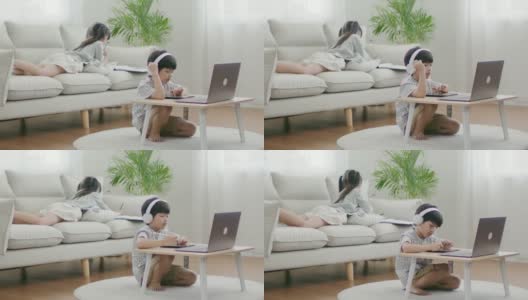 可爱的兄弟姐妹在舒适的客厅里一起学习在线课程。高清在线视频素材下载