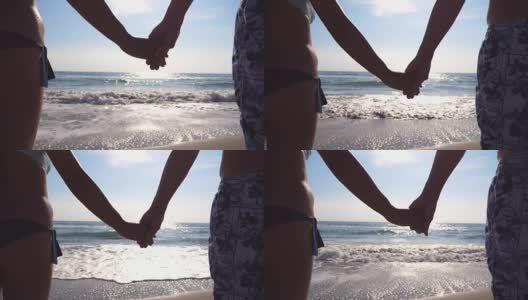 年轻的情侣站在海边，欣赏美丽的风景。在海滩上，男性和女性的手臂互相爱抚。暑假或假期。近点后视图高清在线视频素材下载