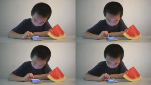 亚洲男孩坐在桌子前，高兴地吃着西瓜高清在线视频素材下载