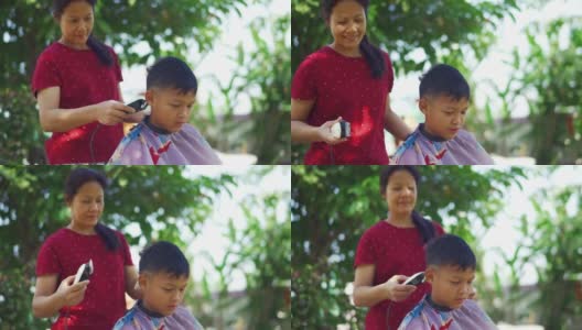 亚洲母亲正在修剪她的儿子的头发在早上在花园里。在COVID-19或冠状病毒大流行期间的国内高清在线视频素材下载