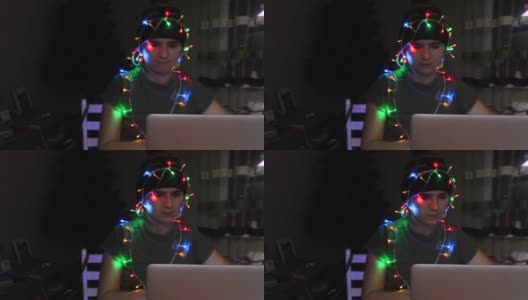 离焦点的年轻女子庆祝圣诞节工作在笔记本电脑，有乐趣在冬季假期的彩灯，包裹在花环。黑夜里的圣诞。假日。累了。的焦点高清在线视频素材下载