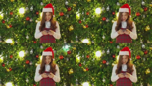 快乐女人用智能手机与圣诞树，欢度圣诞高清在线视频素材下载