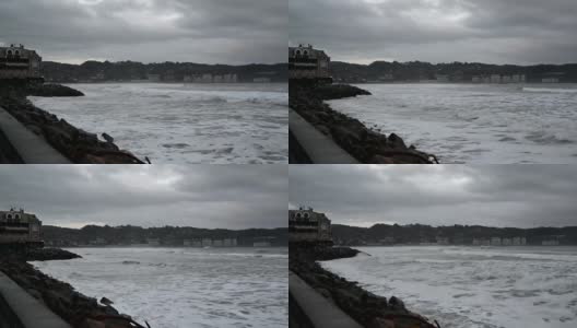 在法国亨达耶，背景是亨达里比，一个灰色的多云的日子，海浪汹涌，海浪拍打着码头的岩石，使海滩消失。白色的泡沫和铅灰色的日子高清在线视频素材下载