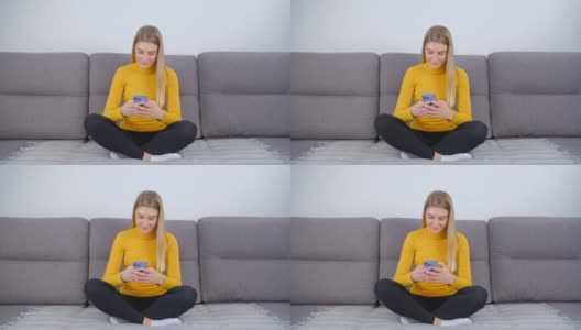 快乐的金发女人在手机上留言。禁闭期间，一名快乐的白人女性坐在家里的沙发上，用现代手机进行交流。微笑的人在线交流高清在线视频素材下载