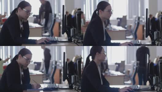 冷漠，不快乐的女商人戴着眼镜坐在办公室的桌子上用电脑工作高清在线视频素材下载