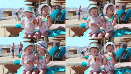 两个小女孩在海滩上吃牛角面包。沙姆沙伊赫。埃及。高清在线视频素材下载