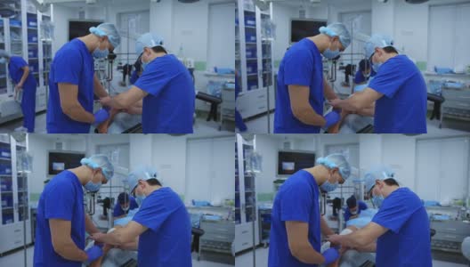 手术的腿。在现代化的手术室里，穿着蓝色制服的医学专家正在给躺在手术台上的病人做手术。高清在线视频素材下载