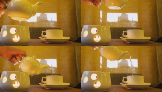 男手拿水壶，站在蜡烛上，在茶杯上倒热茶高清在线视频素材下载