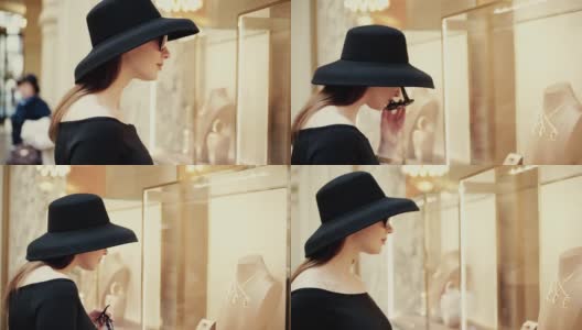 一位年轻漂亮的女士戴着帽子和太阳镜走到一家精品店的橱窗前，兴致勃勃地看着商品。奢华珠宝商店高清在线视频素材下载