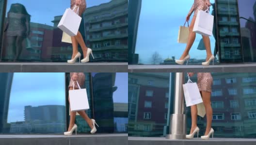 美丽的腿在鞋跟鞋沿着玻璃商店的橱窗。性感的腿特写。漂亮的年轻女孩穿着红色的衣服，手里拿着购物袋享受美丽的天气高清在线视频素材下载