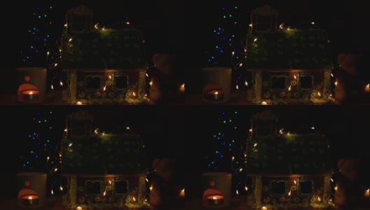 用软熊装饰自制的甜饼屋，在香薰灯中点缀发光的蜡烛，散光的节日花环装饰模糊了圣诞树的散光灯的黑暗背景。新年前夜4K视频高清在线视频素材下载