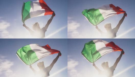 夕阳西下的意大利海滩上，一个年轻人双手举着意大利国旗向天空飞翔高清在线视频素材下载