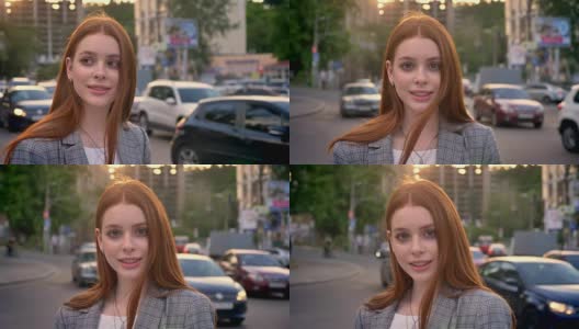 年轻迷人的女子与姜黄色头发站在街上，看着镜头在日落，微笑，车辆的背景高清在线视频素材下载