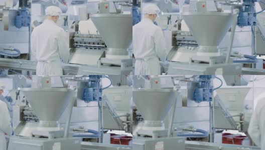 两名年轻男性食品传送带员工在饺子厂工作。他们背对着镜头站在生产线上做体力劳动。他们戴着白色的卫生帽和工作袍。高清在线视频素材下载