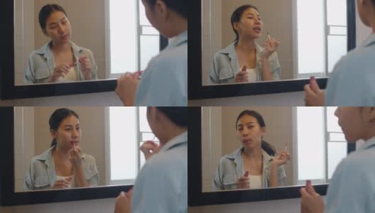 美丽的亚洲女人在镜子前用口红化妆，快乐的中国女性使用美容化妆品提高自己准备在家里的浴室工作。生活方式女性在家放松的概念高清在线视频素材下载