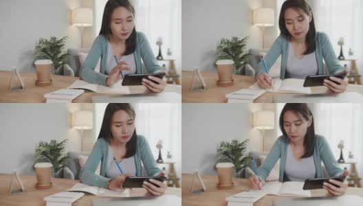 亚洲女性自由职业者使用智能手机检查电子邮件，阅读商业报告，同时在笔记本上做笔记，在家办公高清在线视频素材下载