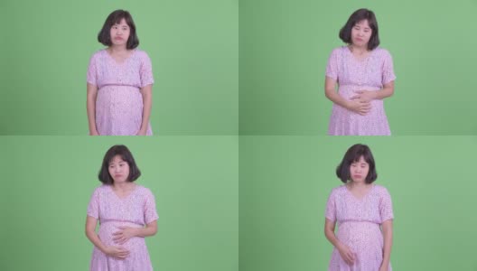 摄影棚拍摄美丽的怀孕亚洲妇女看起来无聊的绿色摄影棚背景高清在线视频素材下载