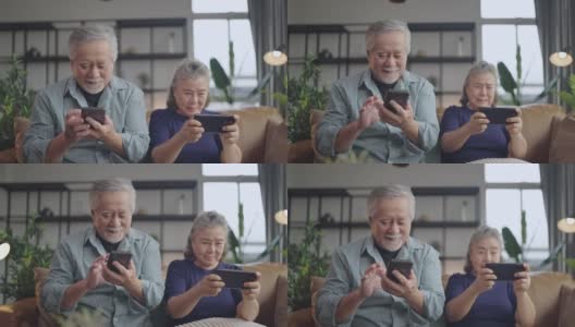 幸福亚洲退休夫妇在客厅家中室内的沙发上一起享受玩游戏和竞争游戏智能手机在线，亚洲夫妇一起玩游戏家隔离的想法高清在线视频素材下载