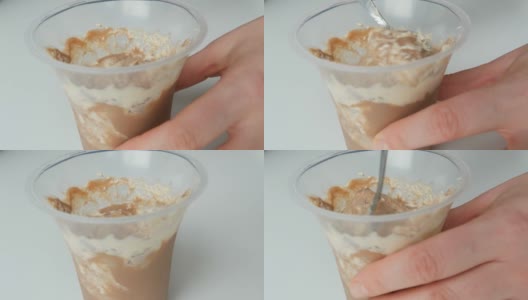用塑料杯装掼奶油和巧克力的甜点。女性用茶匙搅拌顶部的奶油高清在线视频素材下载