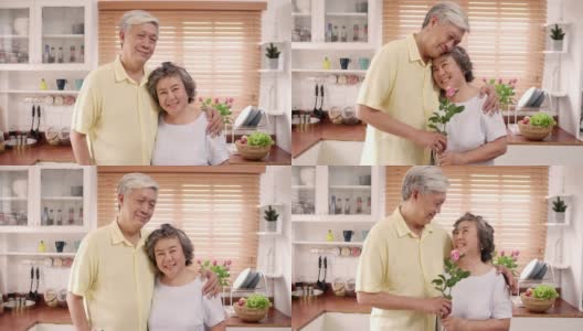 亚洲老夫妇感到幸福的微笑，拿着花，看着镜头，而放松在厨房在家里。生活方式老年人家庭享受居家时光的概念。看着相机的人像。高清在线视频素材下载
