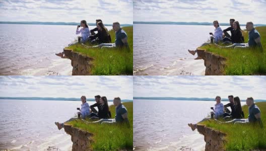 快乐的朋友们，坐在河边的小山上，休闲饮茶高清在线视频素材下载