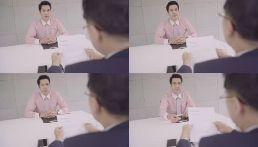 慢镜头——迷人的年轻亚洲商人在面试中与正在看他简历的公司人事经理。一名亚洲商人正在面试一名男性求职者。高清在线视频素材下载