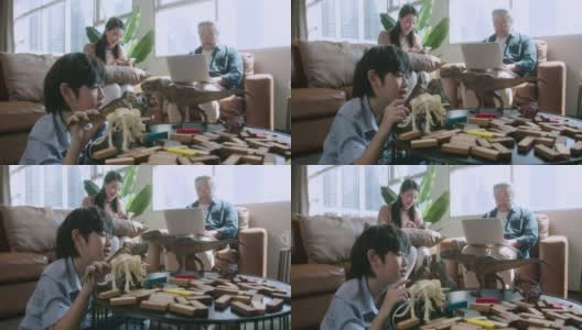 幸福的儿子孩子玩而父母一起放松在家里的沙发，微笑活跃的男孩娱乐与玩具恐龙在地板上，幸福的家庭花时间在客厅在周末高清在线视频素材下载