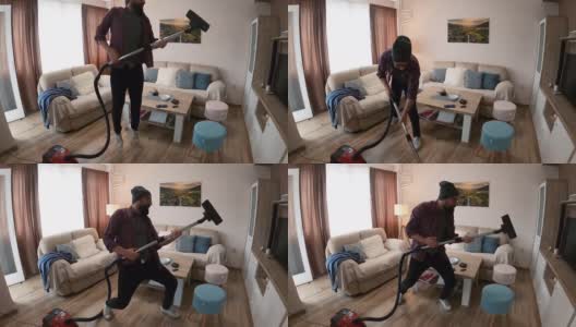 男人在家里拍自拍视频。一个快乐的男人穿着现代风格的衣服，一边用吸尘器打扫公寓，一边唱歌和玩耍。高清在线视频素材下载