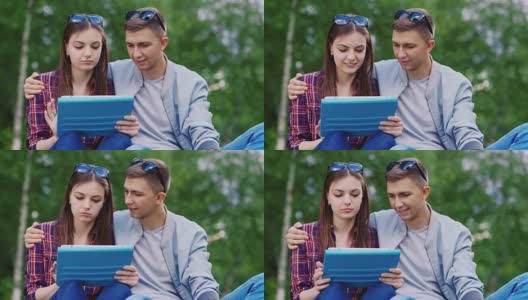 年轻女孩和一个男孩在公园里用平板电脑，男孩拥抱女孩高清在线视频素材下载